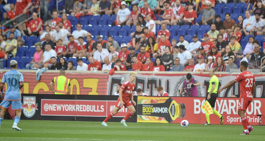The New York Red Bulls playing the ball down the sideline, building their attack against New York City FC. Forward Tom Barlow of the Red Bulls and Midfielder Cristian Cásseres of the Red Bulls. Defending the play is City midfielder Santiago Rodriguez(10).  