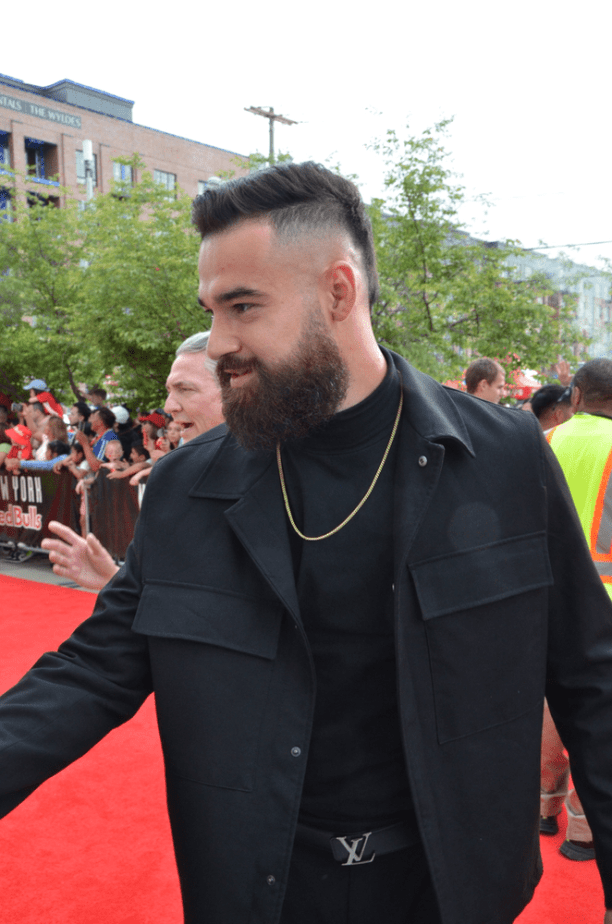 Carlos Coronel with a beard wearing a black outfit walks on a red carpet, surrounded by fans and greenery in the background entering Red Bull Arena after the red carpet team walk in.