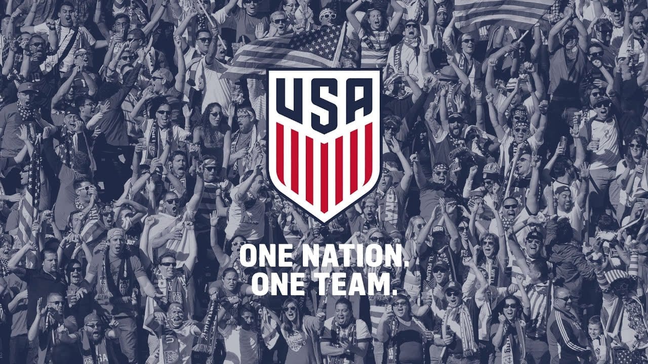 US Soccer logo with "One Nation. One Team." slogan overlaid on crowd of American soccer fans waving flags