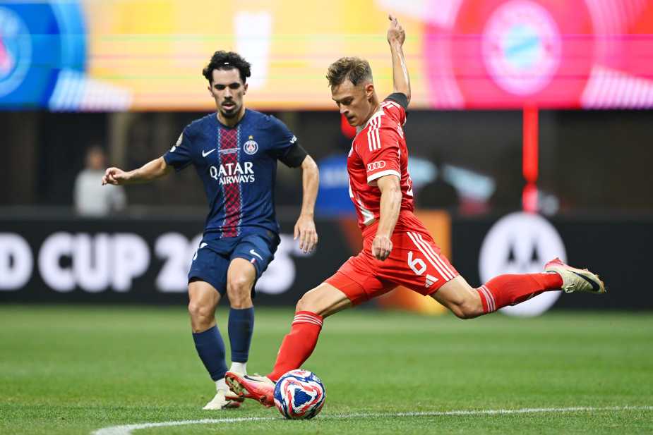 A Bayern Munich player in a red kit takes a shot while a Paris Saint-Germain player in a navy kit closely defends during a match.