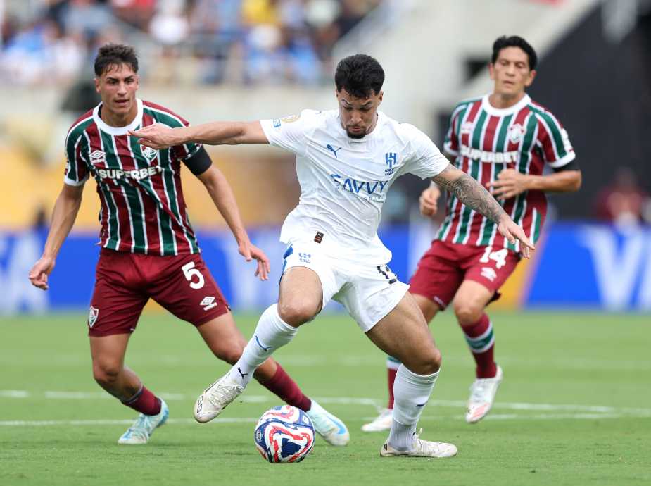 A player from Al Hilal in a white jersey dribbles the ball while being pursued by two players from Fluminense, who are wearing maroon and green striped jerseys.