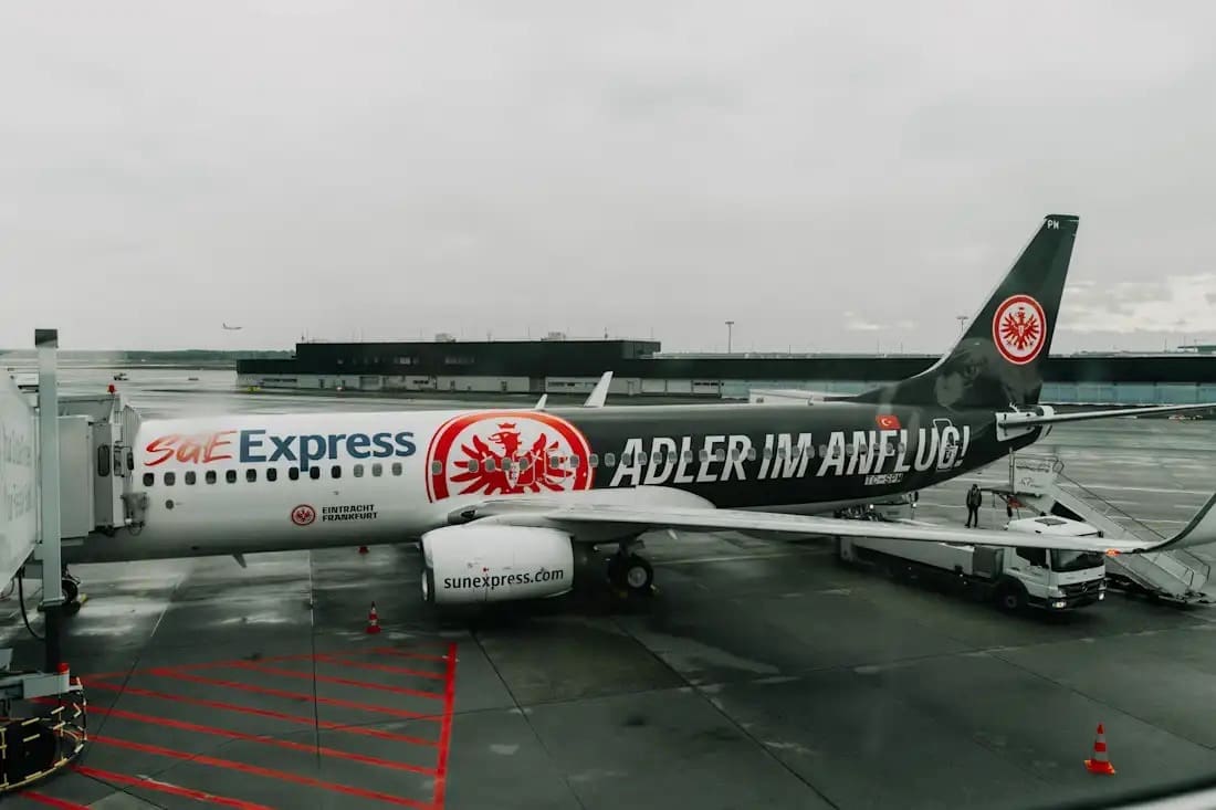 A SunExpress aircraft featuring Eintracht Frankfurt branding, parked at an airport gate with ground crew preparing for departure.