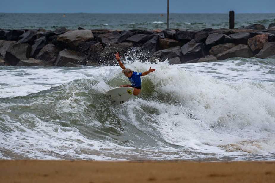 Ella McCaffray executes a powerful cutback maneuver in whitewater during her championship-winning performance at the 2025 Virginia Beach Pro, with rocky jetty visible in background