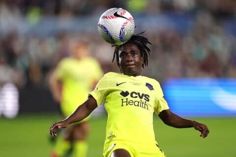 Rosemonde Kouassi in bright yellow CVS Health jersey heads the ball during NWSL match with crowd in background