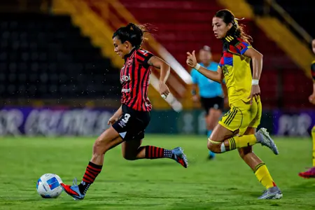 LD Alajuelense player in red and black striped jersey dribbles past Club América defender in yellow during 0-0 Concacaf W Champions Cup match at Estadio Alejandro Morera Soto