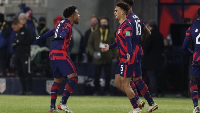 Two USMNT players in red and blue striped jerseys celebrate together after scoring goal during international match