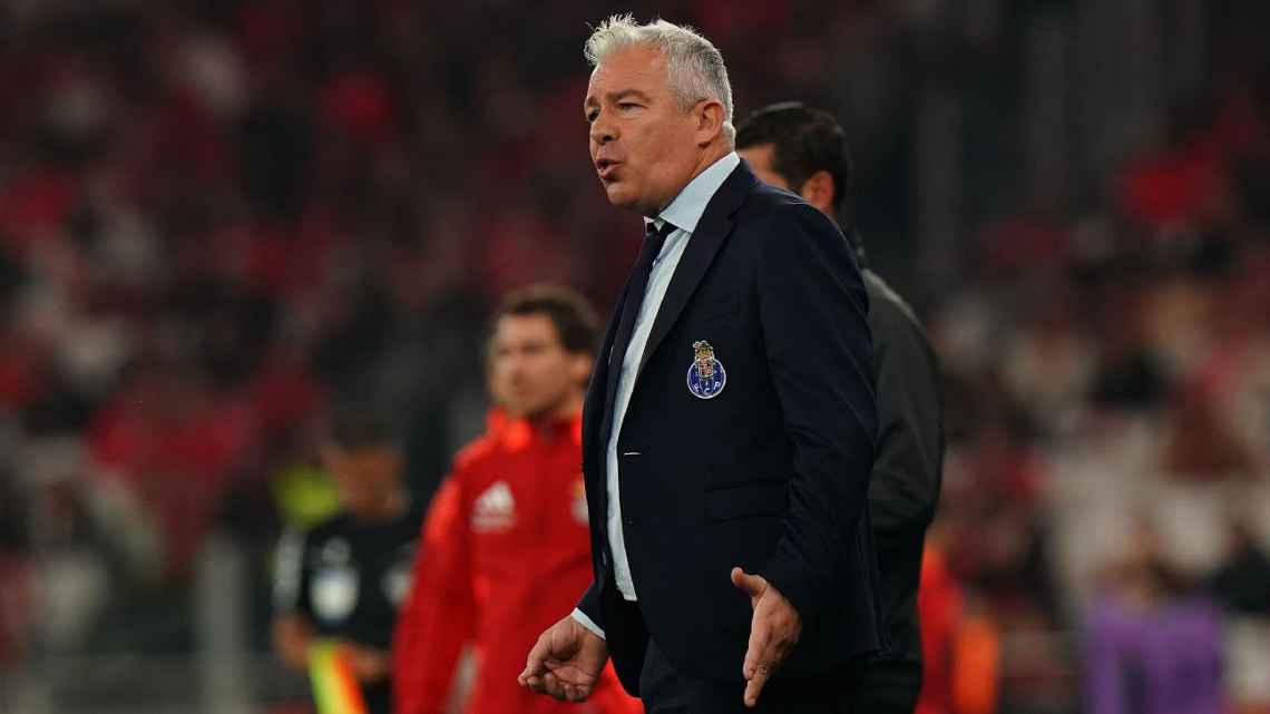 FC Porto coach in dark suit stands on sideline during match with Porto crest visible on jacket