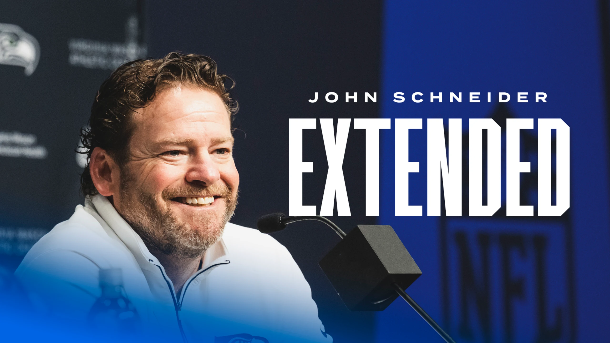 John Schneider smiling at press conference podium with "JOHN SCHNEIDER EXTENDED" text overlay announcing Seattle Seahawks GM contract extension