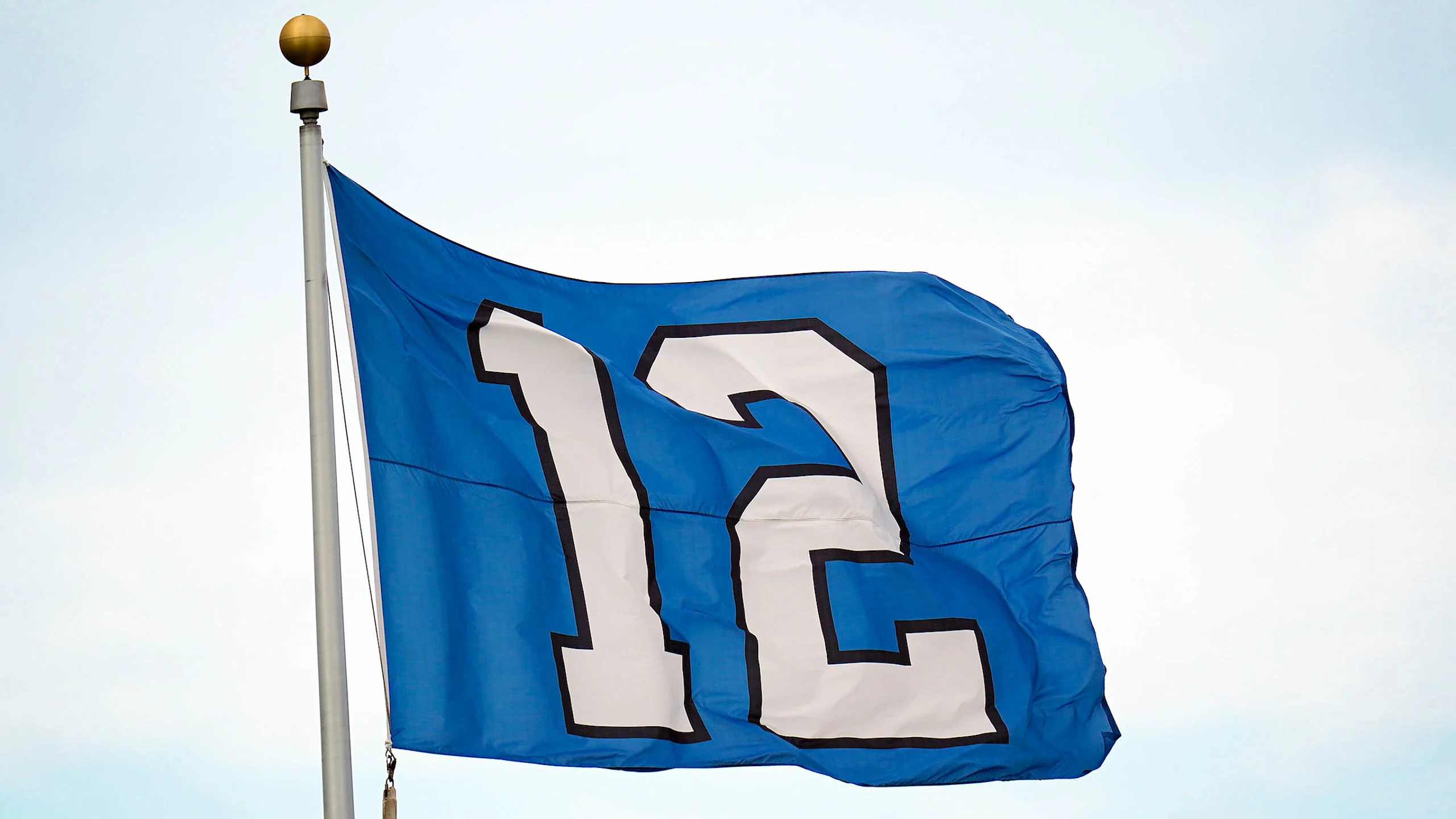 Blue Seattle Seahawks 12th Man flag with white "12" number flying on flagpole against clear sky representing international fan expansion