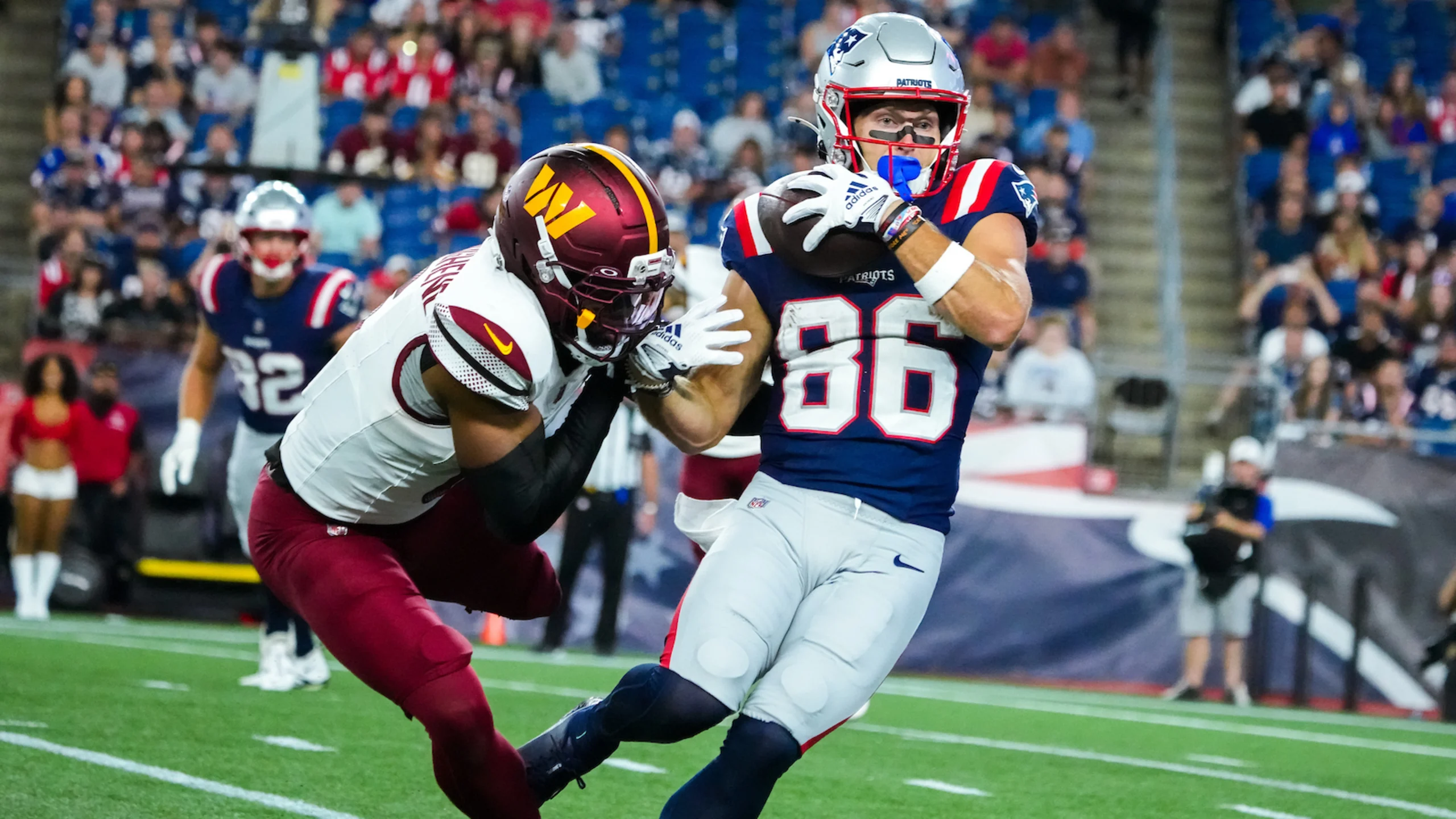 New England Patriots rookie wide receiver Efton Chism (#86) catches pass while being tackled by Washington Commanders defender during preseason game