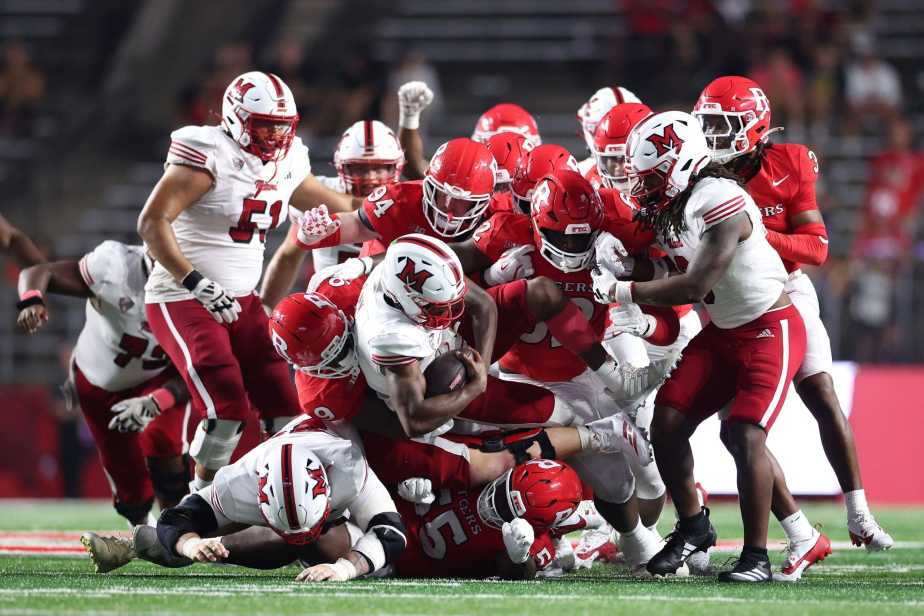 Multiple Rutgers defenders in red jerseys converge to sack Miami (Ohio) quarterback Dequan Finn (#1) in white jersey during a pile-up tackle