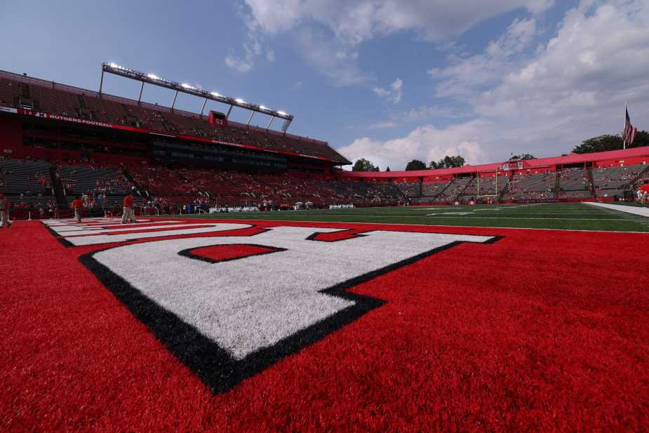Wide-angle view of SHI Stadium's red end zone featuring the large white "R" logo on red turf, with stadium seating and blue sky with white clouds visible in the background