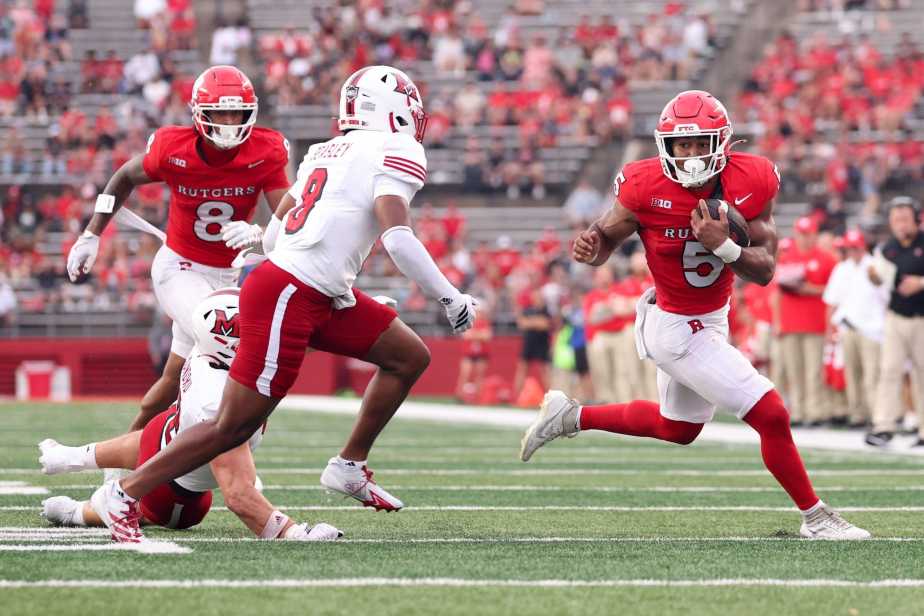 Rutgers running back CJ Campbell Jr. in red jersey number 5 carries the football while evading Miami Ohio defender Koy Beasley in white jersey number 8, with teammate KJ Duff providing blocking support