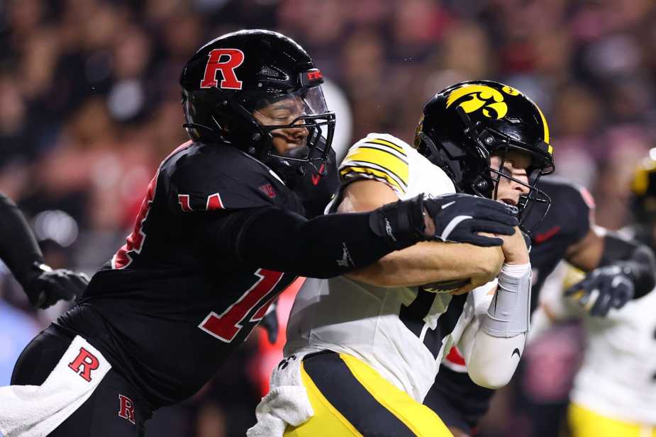 Rutgers defensive lineman #14 Jordan Thompson sacks Iowa quarterback #11 Mark Gronowski, driving him to the ground during an intense defensive play.