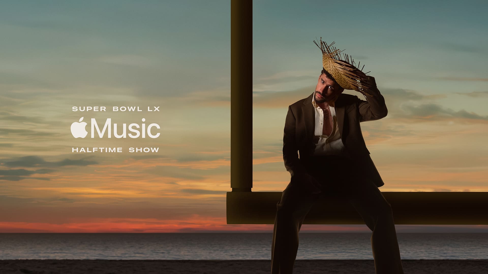 Bad Bunny in black suit wearing traditional straw hat posing against sunset sky for Apple Music Super Bowl LX Halftime Show promotional image