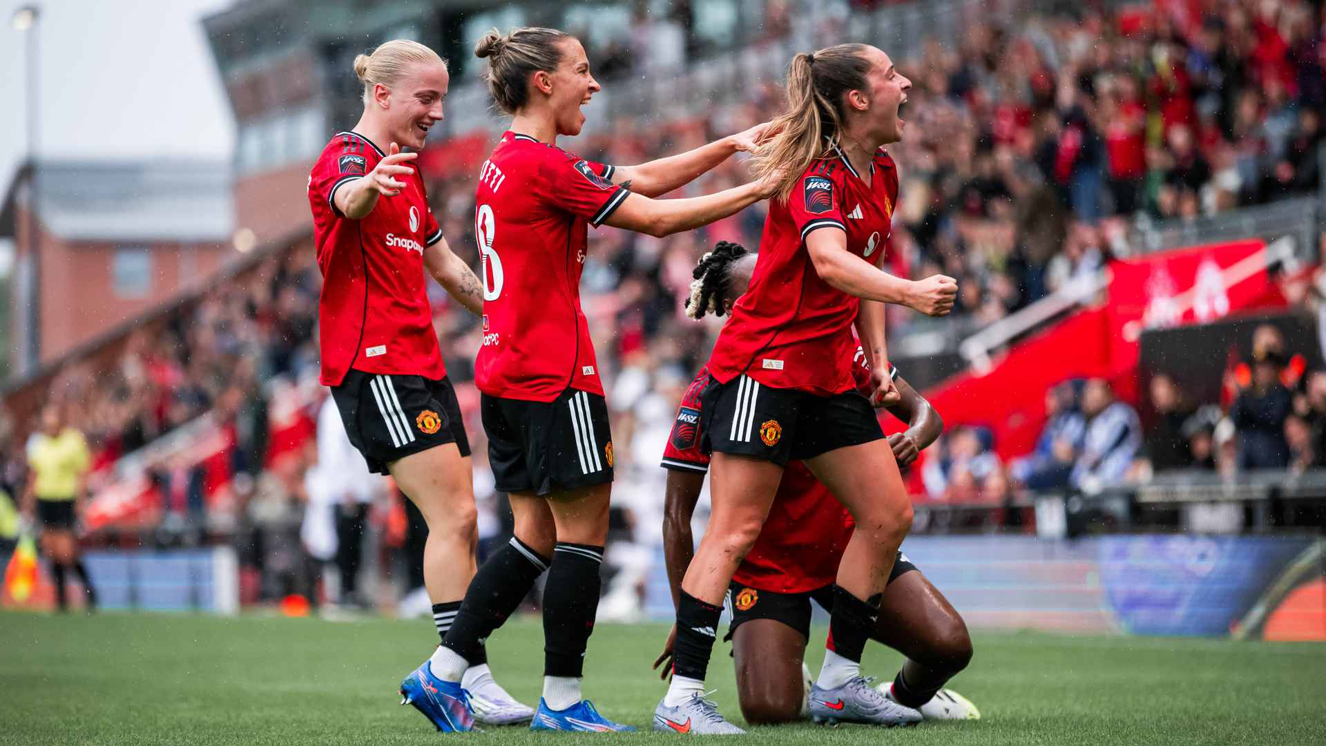 Manchester United Women's players celebrating a goal, wearing red jerseys, with three players in dynamic celebration pose on the football pitch