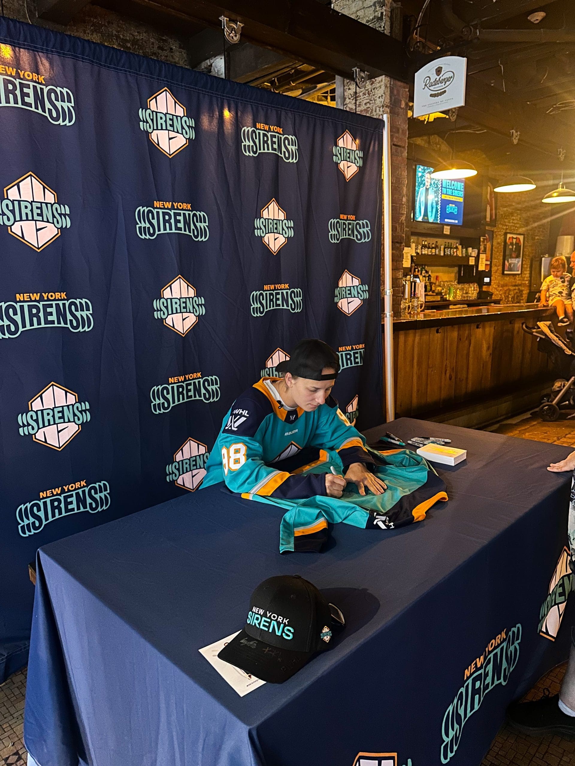 New York Sirens draft pick signing team jersey at autograph table with logo backdrop