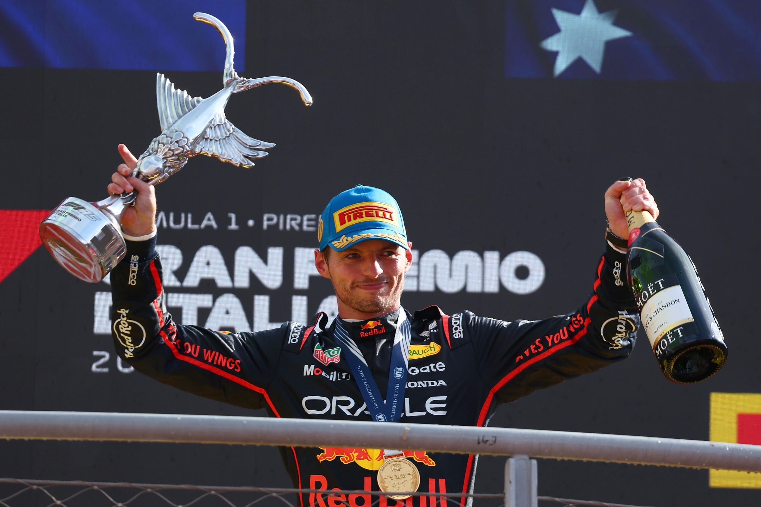 Max Verstappen celebrates on the podium holding the winner's trophy and champagne bottle after his record-breaking victory at the Italian Grand Prix in Monza
