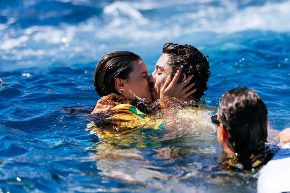 Yago Dora sharing an emotional kiss with a woman in the ocean during his WSL Championship celebration, surrounded by water and support boats