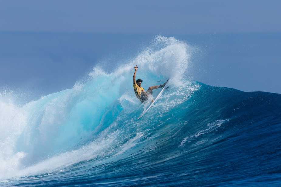 Brazilian surfer Yago Dora executing a dynamic aerial maneuver on a massive turquoise wave during the 2025 WSL Finals in Fiji, wearing a yellow jersey