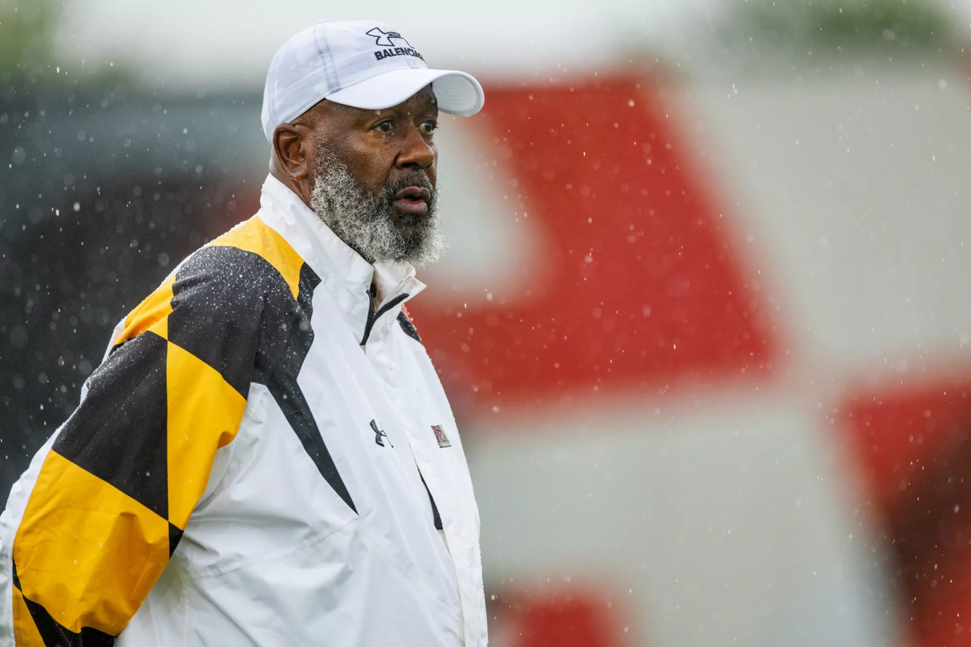 Maryland Terrapins head coach Michael Locksley wearing white Balenciaga cap and team jacket during rainy practice session