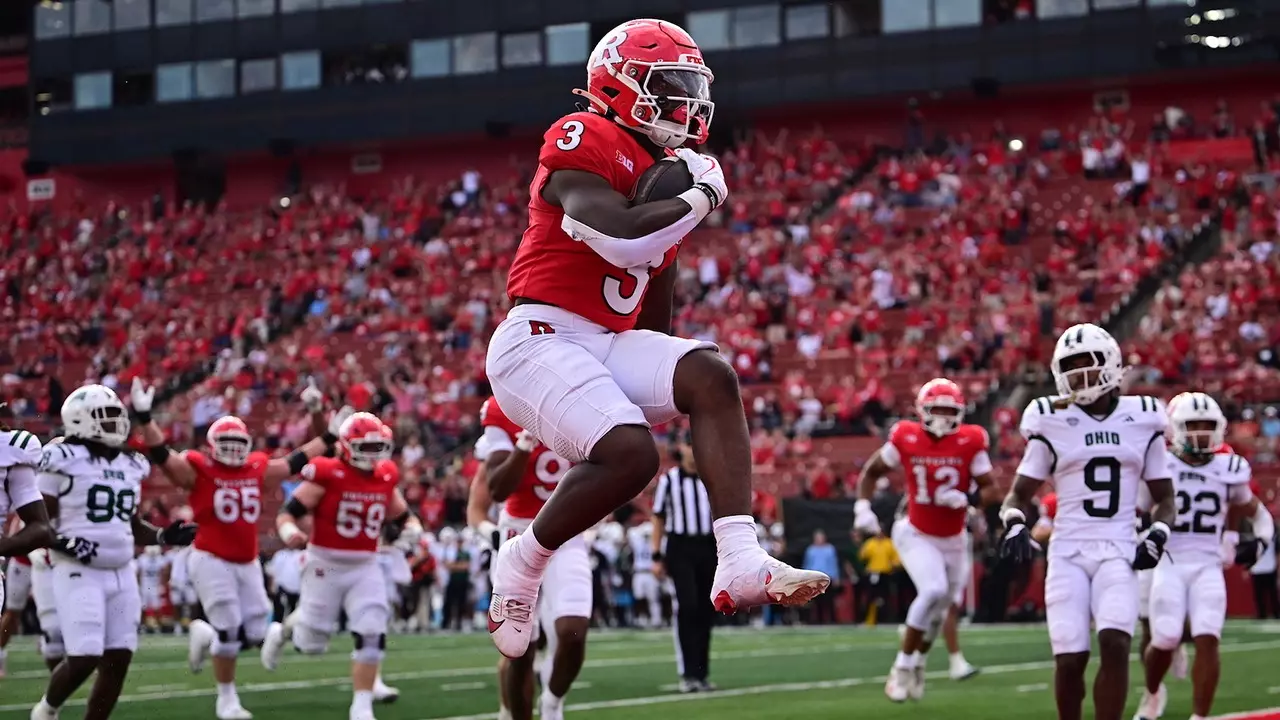 Rutgers running back Antwan Raymond (#3) in red jersey crosses the goal line for a touchdown against Ohio defenders in white jerseys