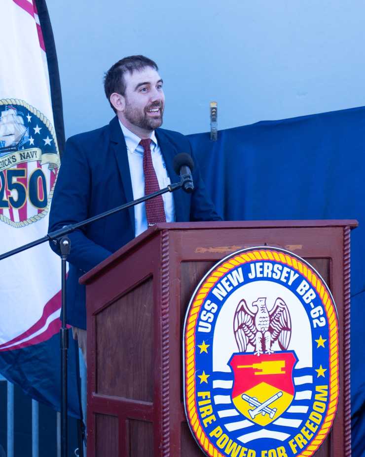Ryan Szimanski, Curator of Battleship New Jersey Museum and Memorial, speaks at USS Enterprise stern plate unveiling ceremony during Navy 250th anniversary celebration on October 10, 2025.