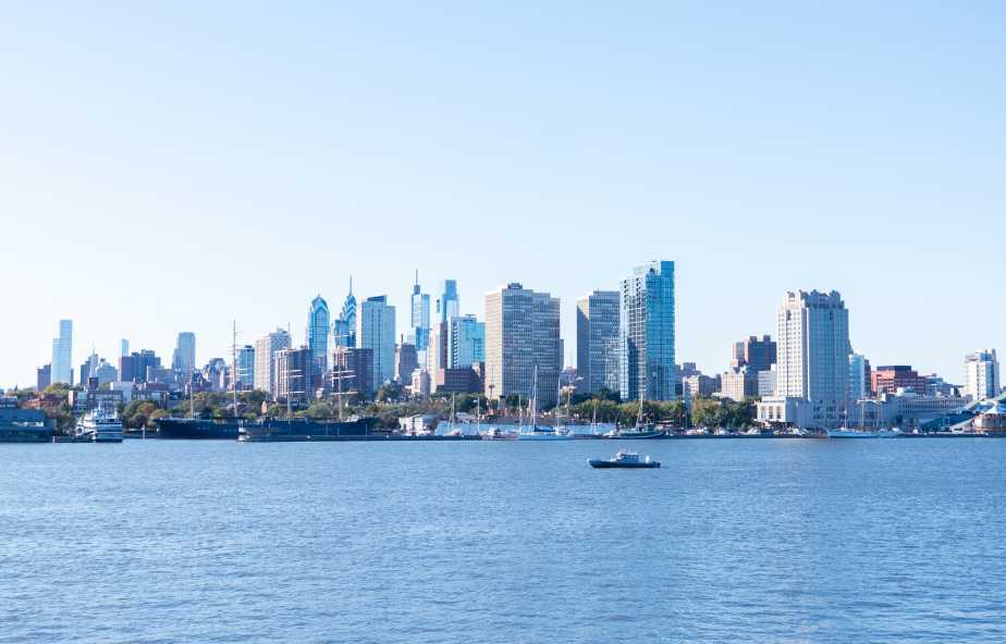 Philadelphia skyline viewed from Camden waterfront across Delaware River during Navy 250th anniversary celebration on October 10, 2025, with small vessel on water.