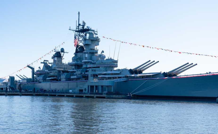 USS New Jersey (BB-62) moored at Camden waterfront displaying ceremonial flags during Navy 250th anniversary celebration on October 10, 2025, with iconic 16-inch gun turrets visible.
