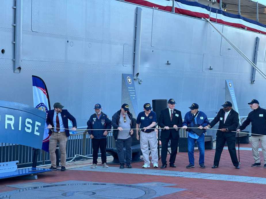 USS Enterprise (CV-6) veterans and family members hold ceremonial ribbon during stern plate unveiling at Battleship New Jersey during Navy 250th anniversary on October 10, 2025.