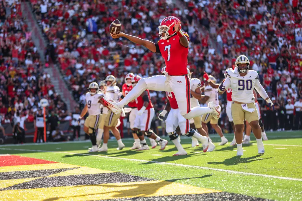 Maryland freshman quarterback #7 Malik Washington runs into the end zone for a touchdown during a game at SECU Stadium, celebrating with arms raised while wearing the Terrapins' red home uniform