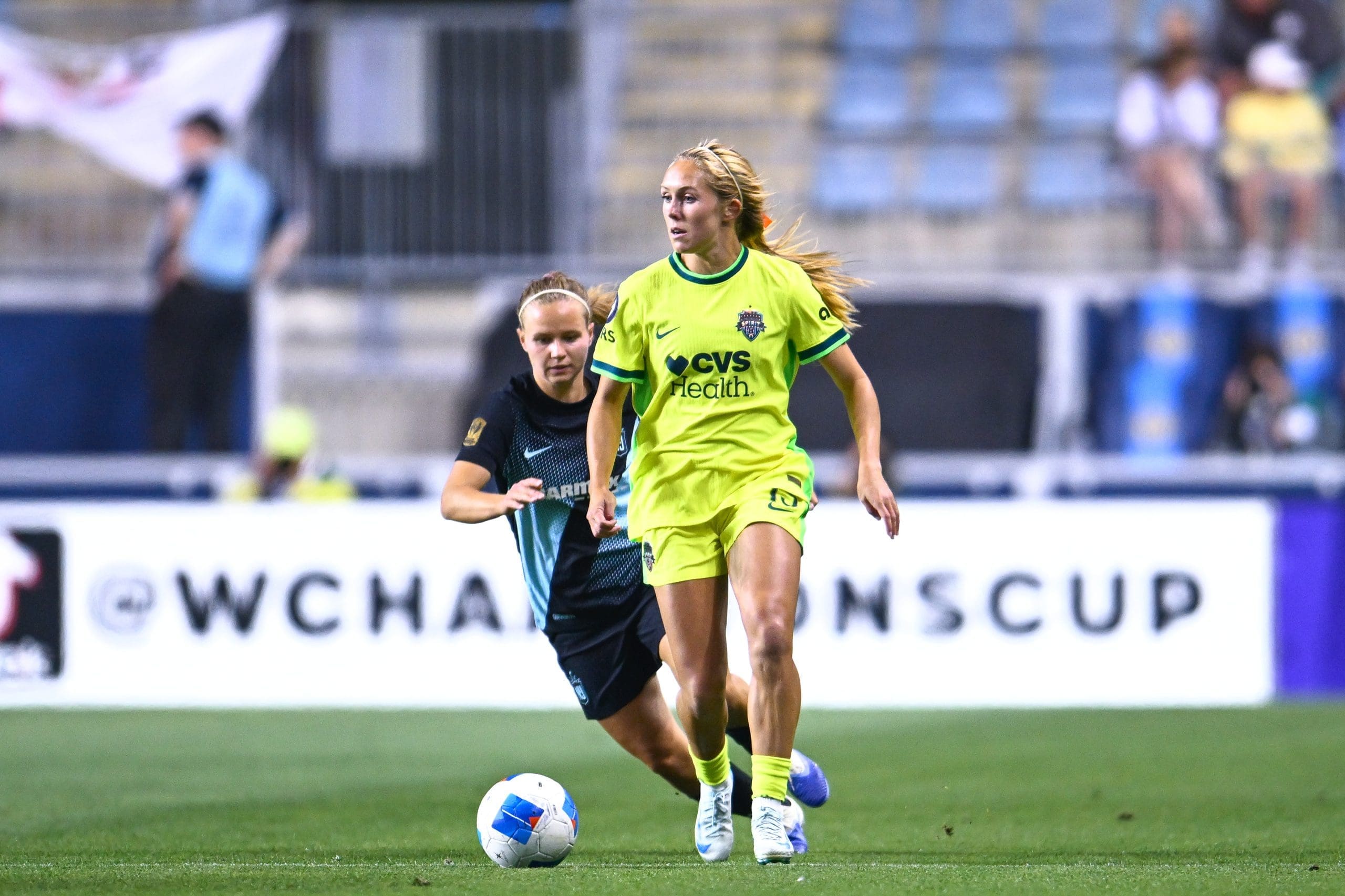 Brittany Ratcliffe, in a bright yellow CVS Health jersey, dribbling a soccer ball during an NWSL/Concacaf Women's champions Cup match, pursued by an opponent at Subaru Park