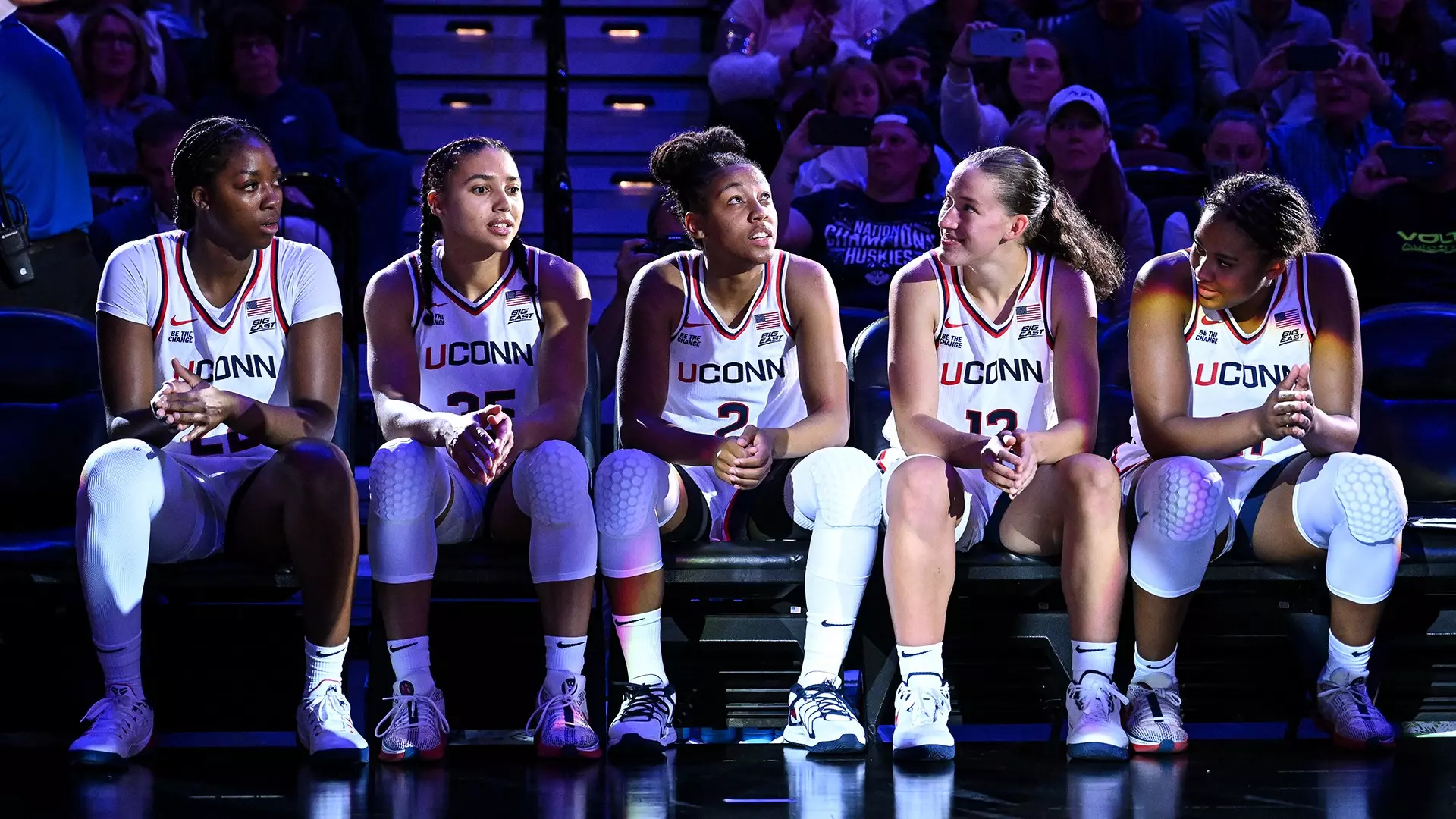 UConn Huskies women's basketball starting five players sitting on bench in white uniforms waiting to be announced before Hall of Fame exhibition game at Mohegan Sun Arena