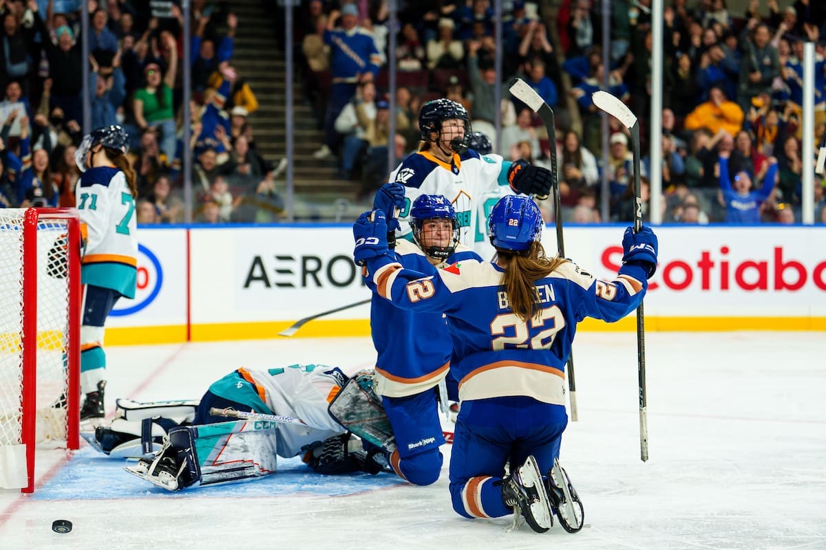 Vancouver Goldeneyes players celebrate a goal against the New York Sirens at Pacific Coliseum, with the Sirens’ goalie down on the ice.