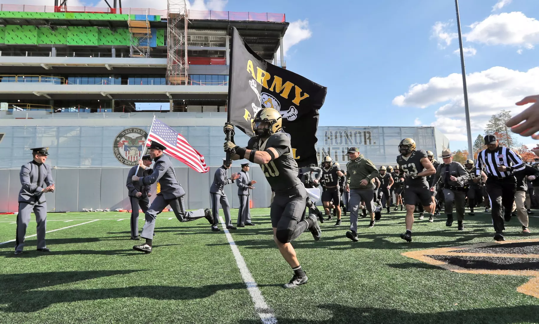 Army Black Knights football team runs onto field at Michie Stadium carrying team flag and American flag