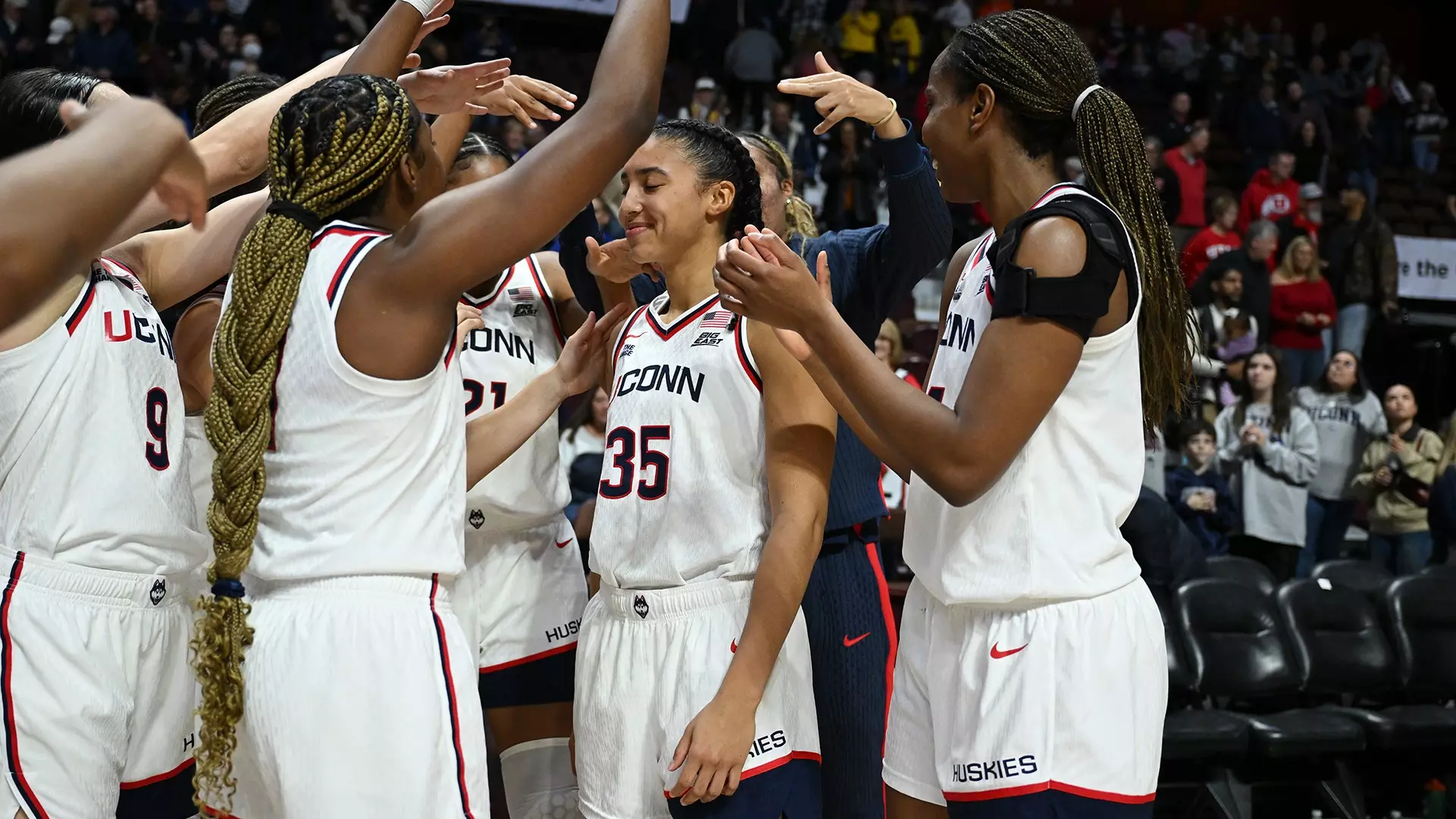 UConn Huskies women's basketball bench players leap from their seats in celebration during their 93-41 victory over Utah at Mohegan Sun Arena, erupting with excitement as teammates dominate the Hall of Fame Women's Showcase
