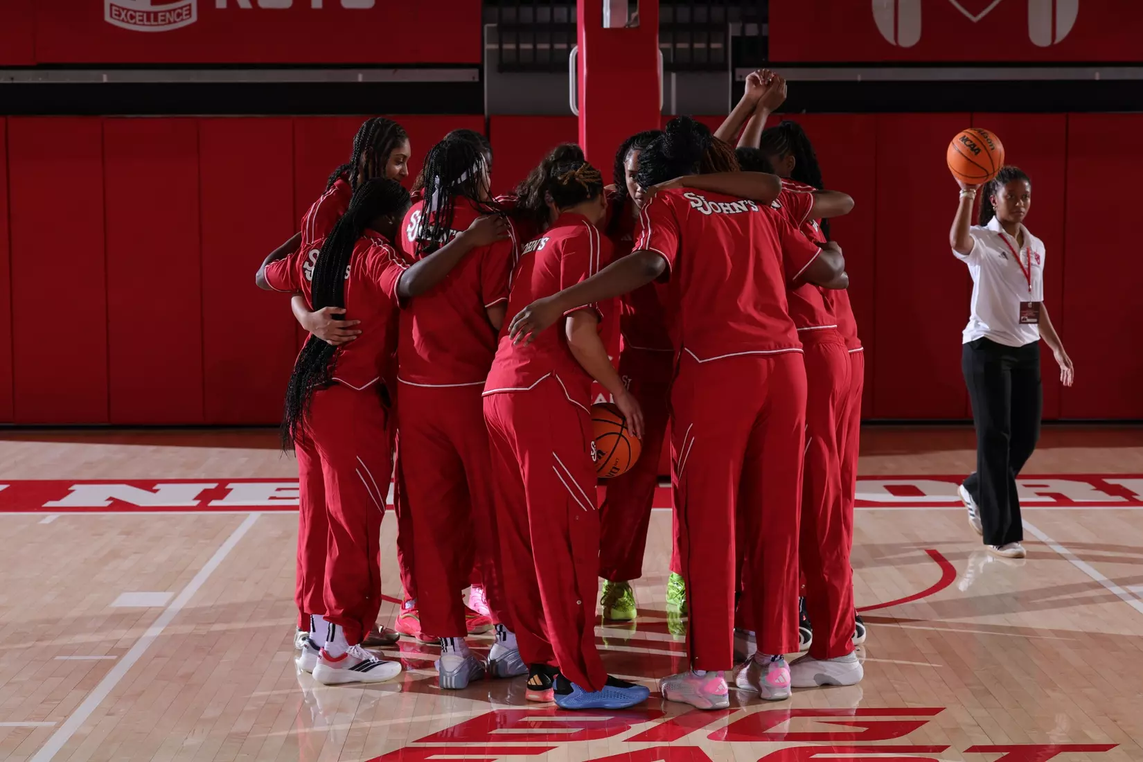 St. John's Red Storm women's basketball team huddles together in red warmup suits at center court before their BIG EAST opener against Creighton at Carnesecca Arena