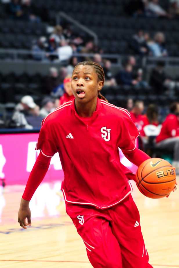 A St. John’s player in a red warmup suit dribbles a basketball during pre-game warmups on the court.