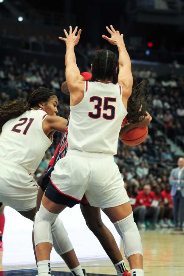 UConn players Sarah Strong (#21) and Azzi Fudd (#35) double-team a St. John’s player in the paint, arms raised, during a defensive stand.
