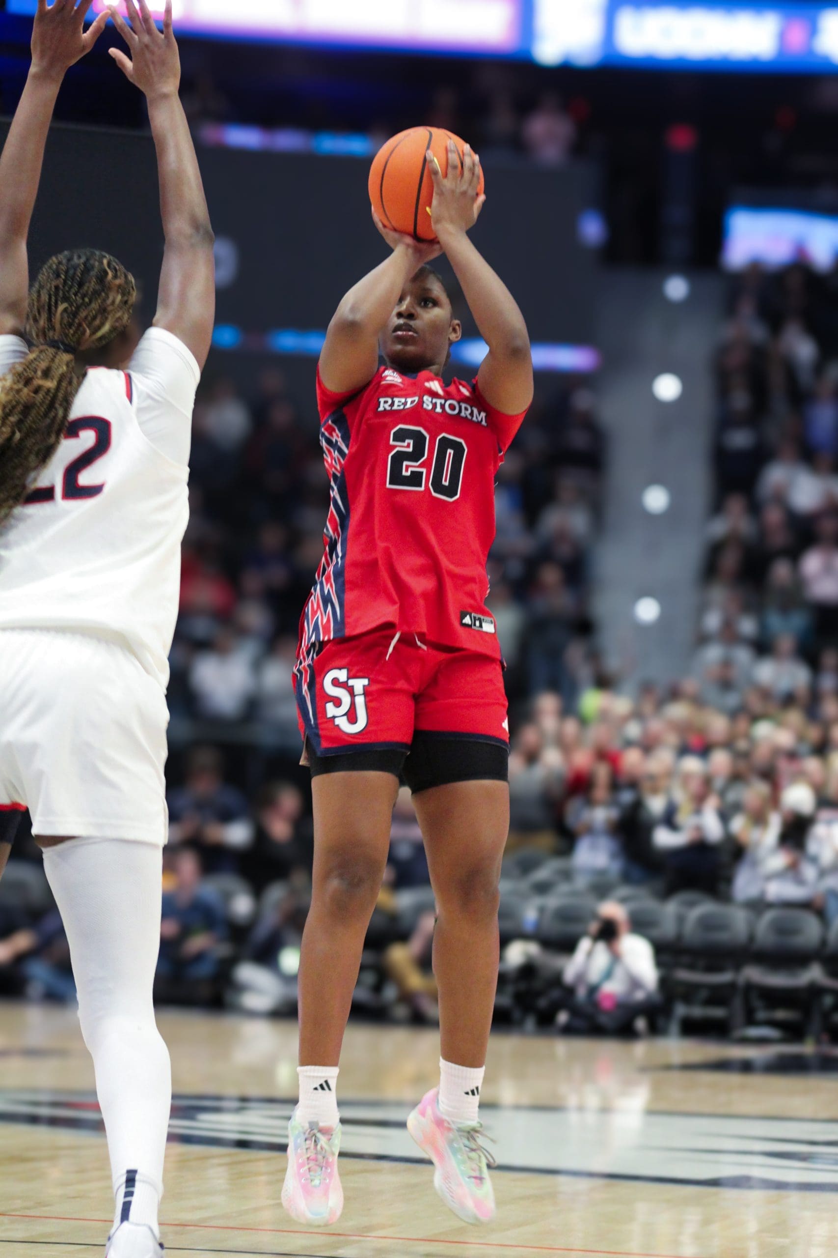 St. John’s Sa’Mya Wyatt (#20) takes a deep jump shot over a UConn defender during a women’s basketball game.