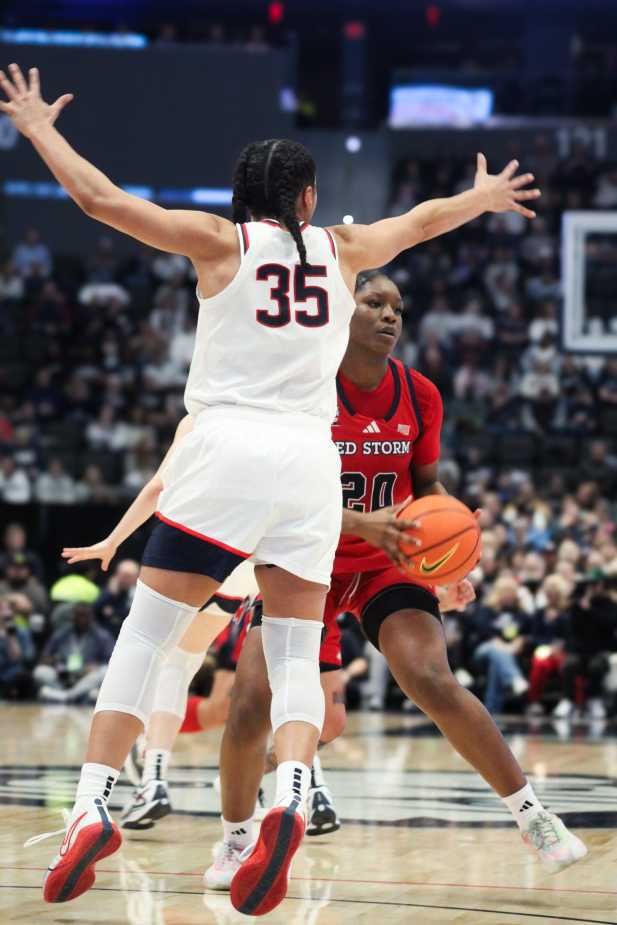 UConn’s Azzi Fudd (#35) raises her arms to defend St. John’s forward (#20) in the paint during a women’s basketball game.