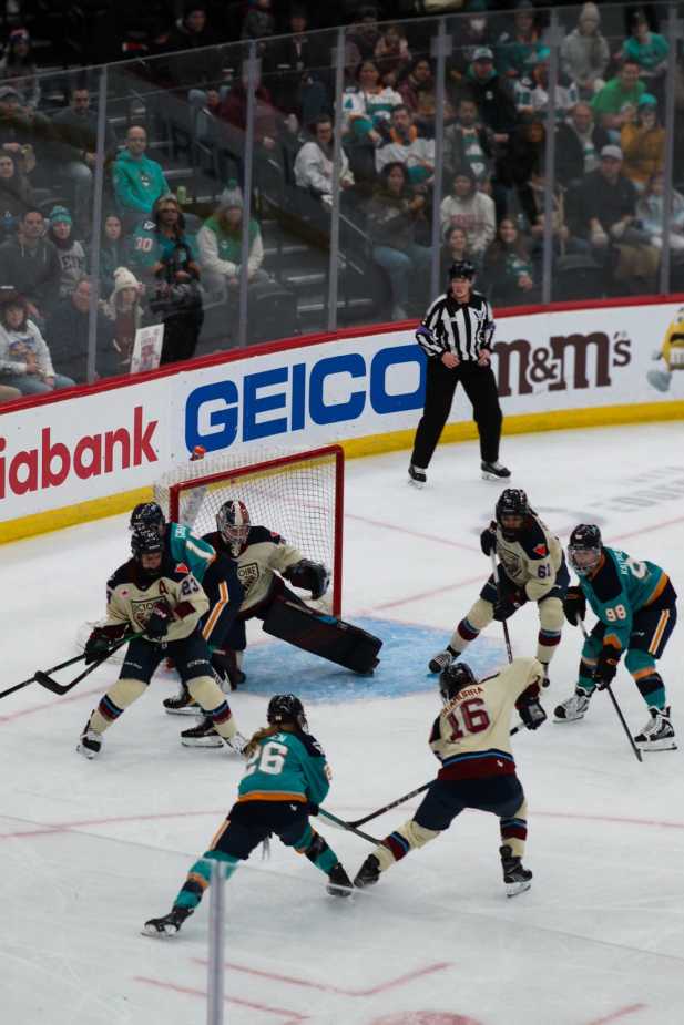 New York Sirens players attack the Montréal Victoire net as multiple Montréal defenders and their goalie work to block the puck during a PWHL game.
