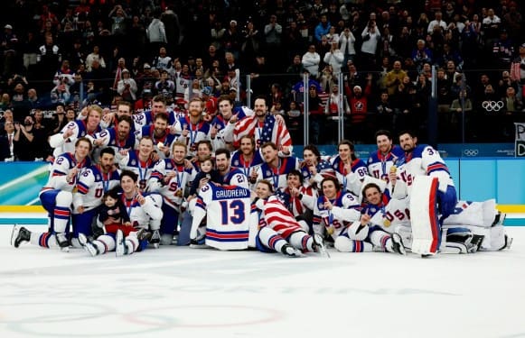 Team USA Men's Hockey poses with the No. 13 Johnny Gaudreau jersey and his children after winning Olympic Gold in 2026.