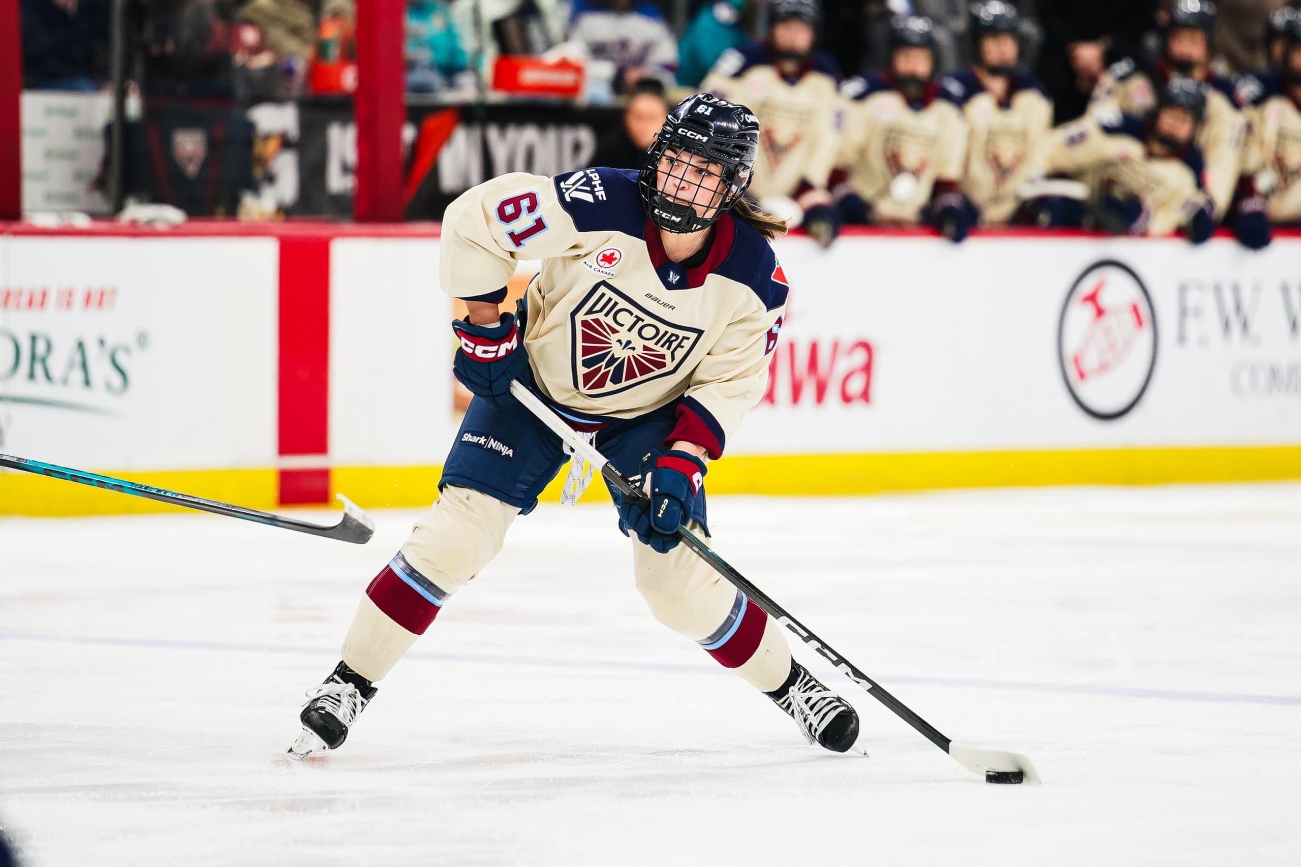 Montréal Victoire defender Nicole Gosling (61) skates with the puck, wearing a cream jersey with maroon and blue accents, during a game against the New York Sirens.