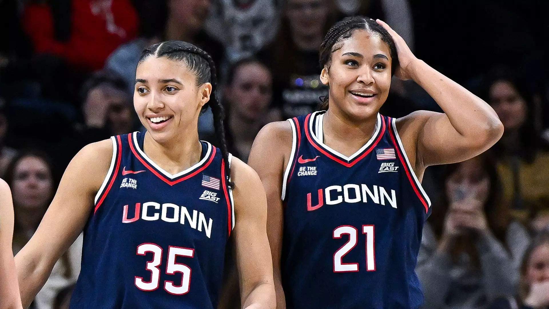 UConn stars Azzi Fudd and Sarah Strong stand together on the court during a game, wearing navy Huskies uniforms.