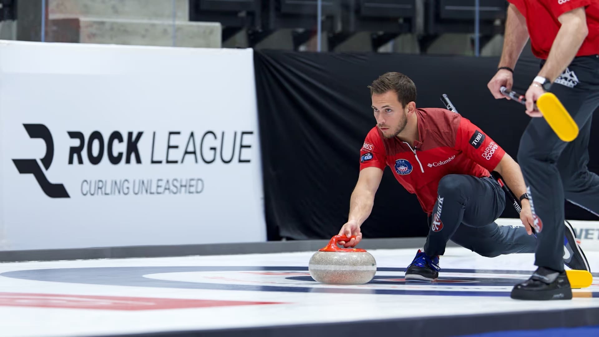 Korey Dropkin, team captain for Frontier in a white, red, and black uniform, delivers a yellow‑handled stone during a match.
