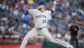 New York Mets left‑hander A.J. Minter delivers a pitch during game action, wearing his gray road uniform with “NEW YORK” across the chest.