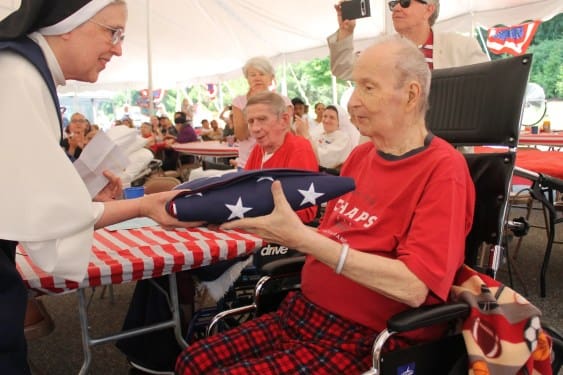A nun from Rosary Hill Home hands a folded American flag to an elderly resident during a ceremony under a white tent.