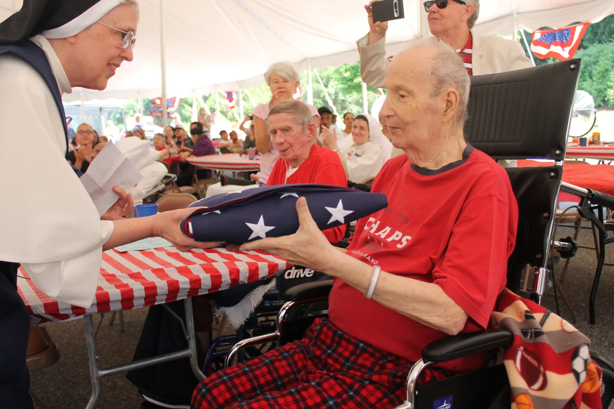 A nun from Rosary Hill Home hands a folded American flag to an elderly resident during a ceremony under a white tent.